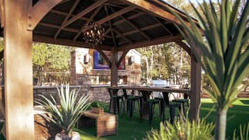 A covered outdoor area with a grill, seating, and a stone wall in the background.