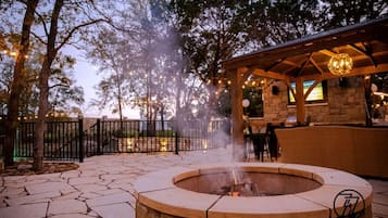 A stone patio with a circular fire pit, outdoor seating, and a stone building with a covered area.