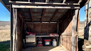 A rustic wooden shed with a metal roof, a workbench, and storage containers. - Wilderness Cabin Rental Perfect for Glamping in Texas (Graford)