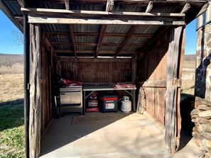 A rustic wooden shed with a metal roof, a workbench, and storage containers. - Wilderness Cabin Rental Perfect for Glamping in Texas (Graford)