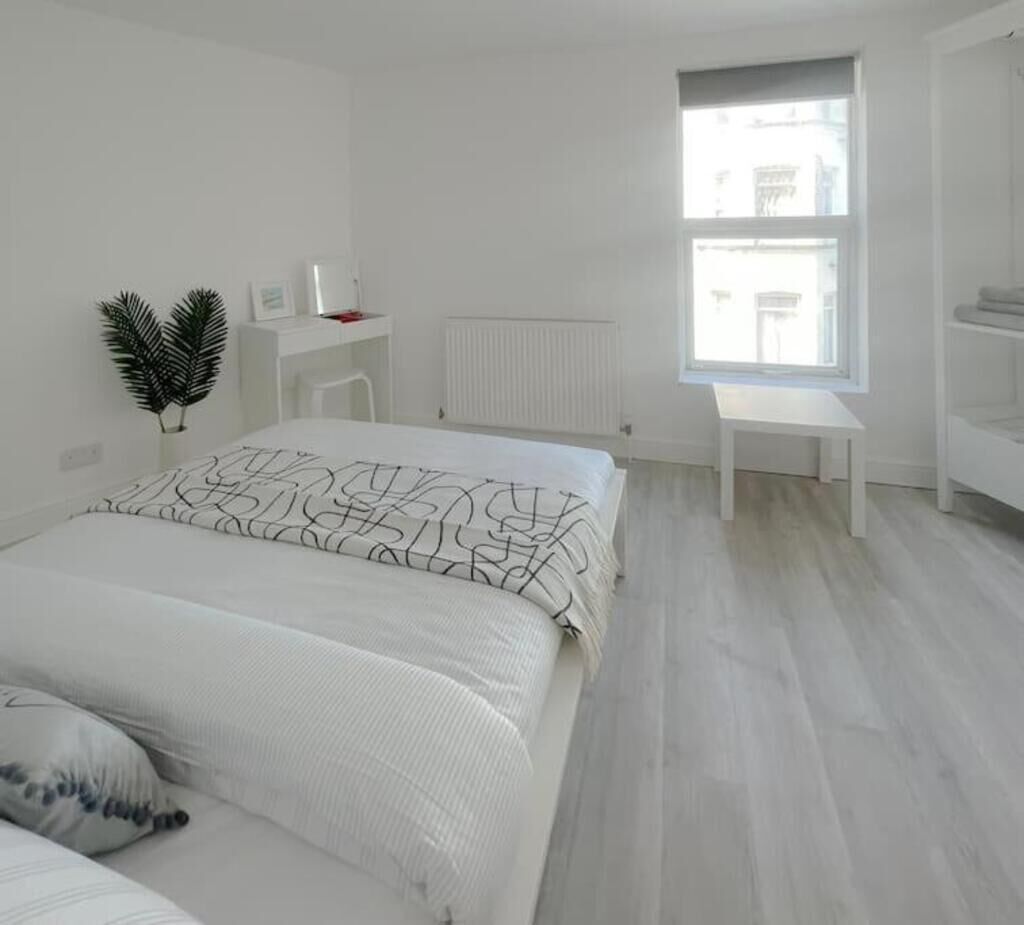 A minimalist bedroom with a large bed, a small desk, a radiator, and a window with a view.