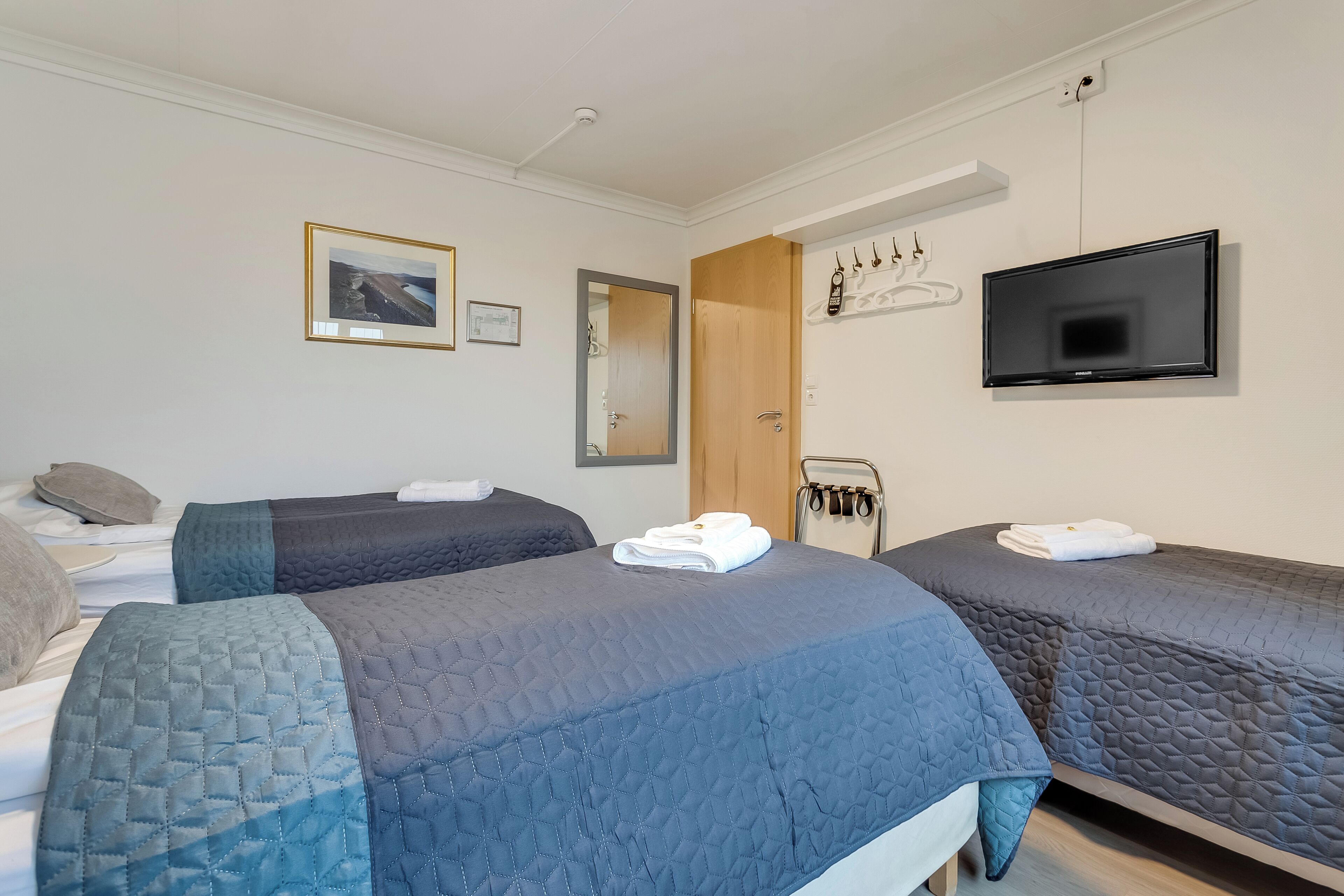 Hotellihuone, jossa on kaksi sänkyä, televisio, peili ja naulakko.