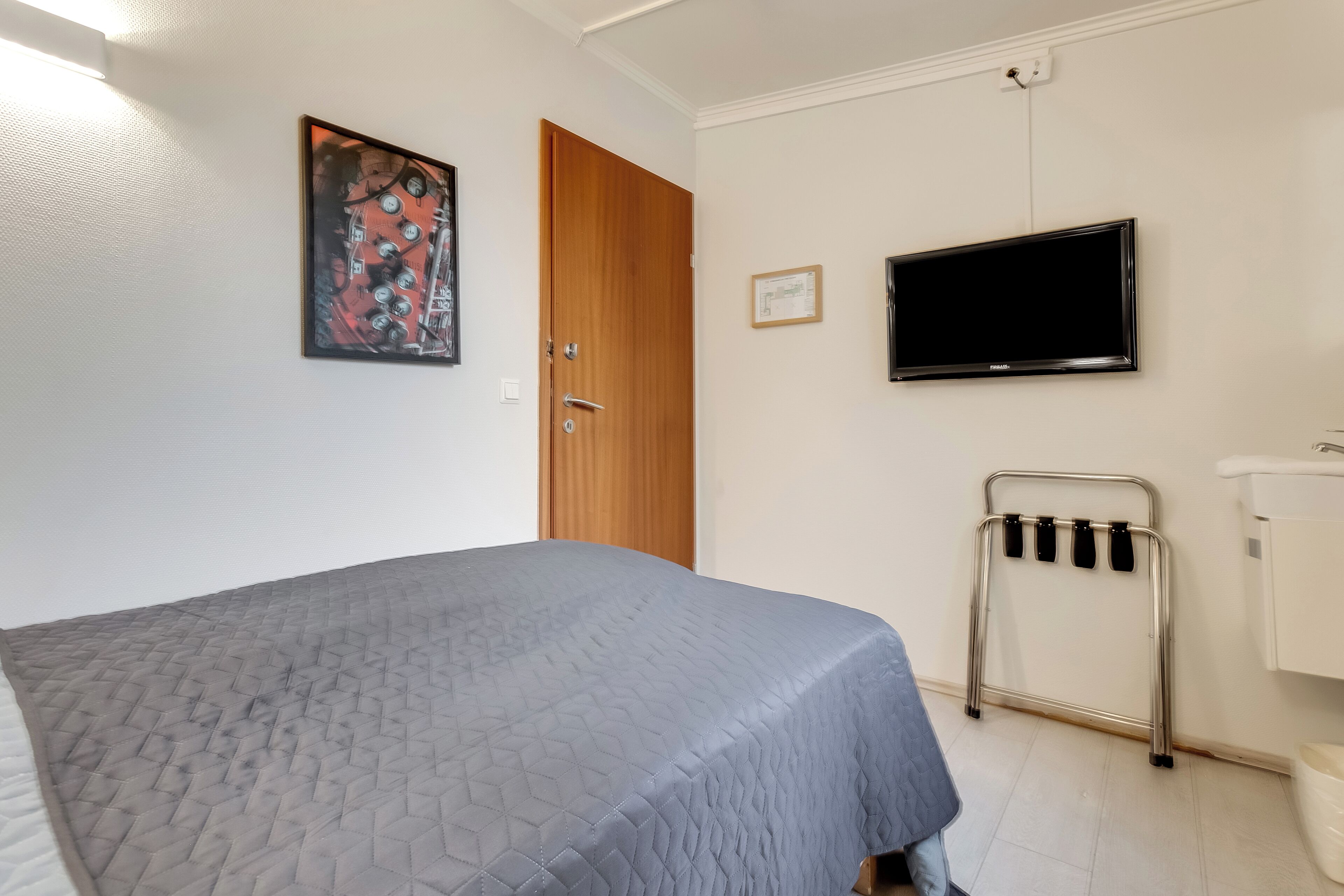 A bedroom with a bed, a wooden door, a television, and a wheelchair.