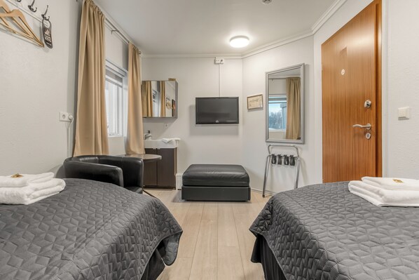Habitación de hotel con dos camas, televisión, espejo, puerta de madera y ventana con cortinas.