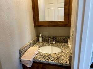 A bathroom with a granite countertop, a white sink, a wooden vanity, a towel, and a mirror above the sink.