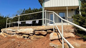 Um edifício com escadas de metal que levam a uma porta, rodeado por pedras e árvores.