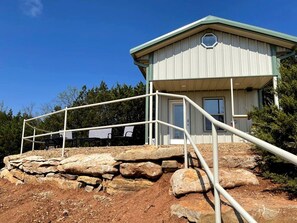 A building with a metal staircase leading to a door, surrounded by rocks and trees.