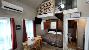 Quarto pequeno com beliches, escrivaninha e uma mesinha.