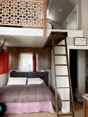Un dormitorio tipo loft con una cama litera, una escalera de madera y un biombo decorativo de madera.