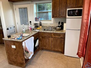 Una cocina con armarios de madera, un refrigerador blanco y un ventanal con vistas a árboles.