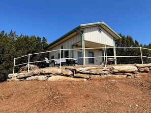 Un edificio de dos pisos con techo plano, un balcón y un muro de contención de piedra.