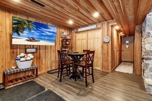 A wooden interior with a dining table, chairs, a TV, a sign, and a wall-mounted shelf with ski boots.