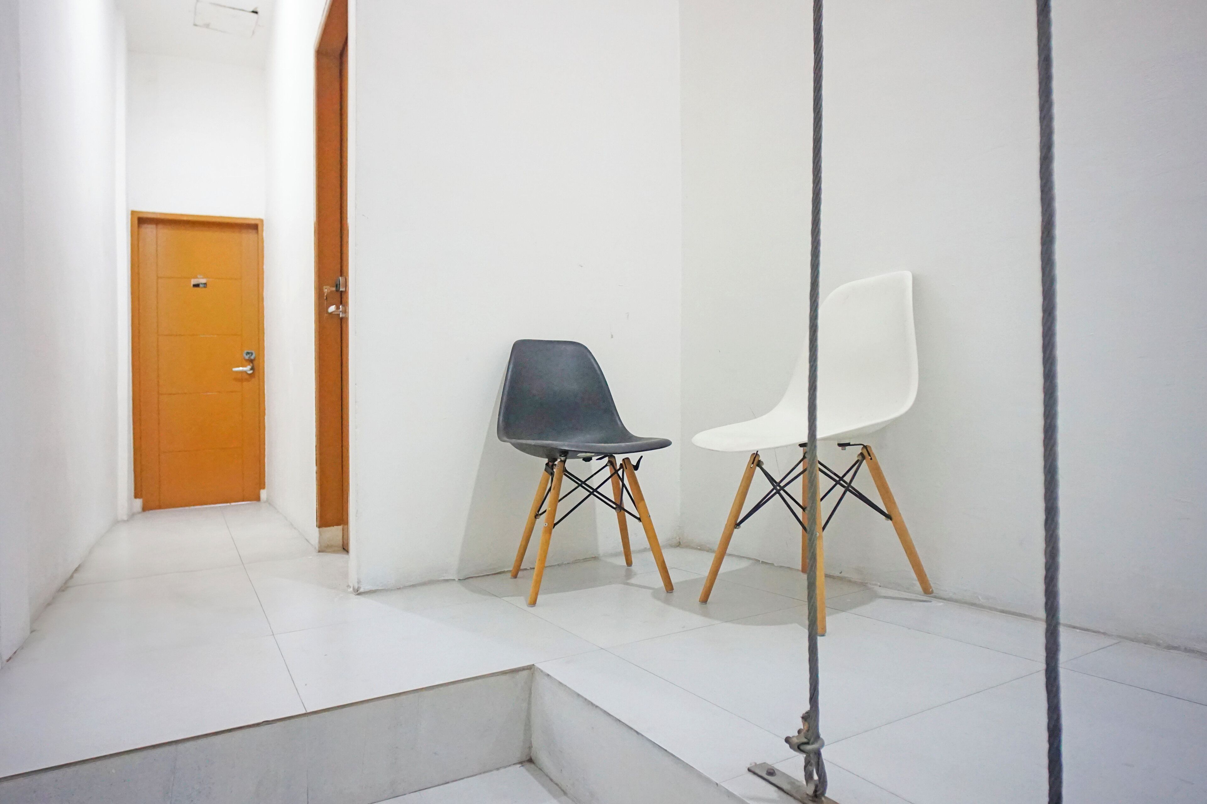 A hallway with a wooden door, two chairs with wooden legs, and a white wall.