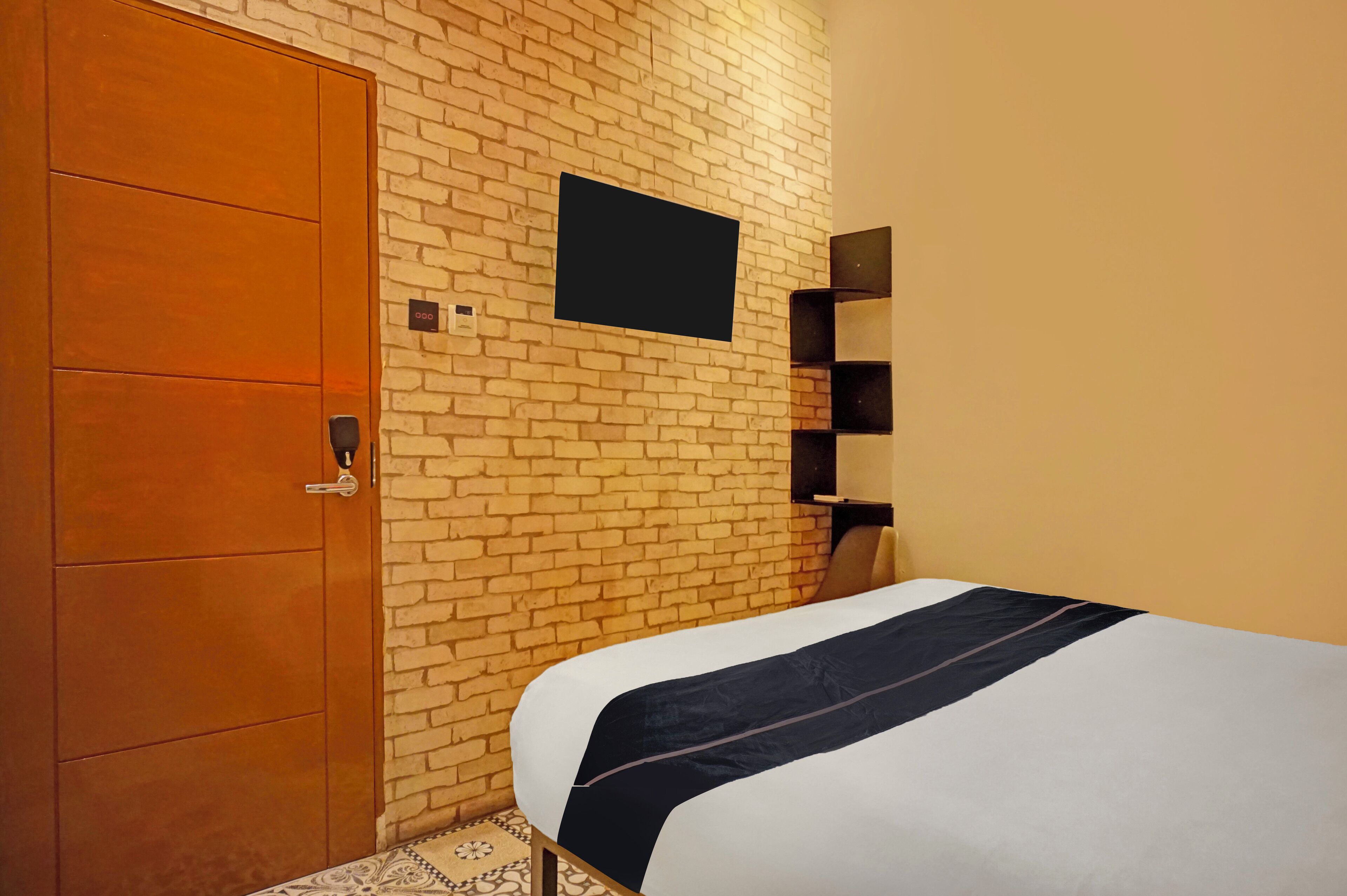 Ein Hotelzimmer mit Backsteinwand, einem Holzschrank, einem Bett mit dunkler Bettdecke und einem an der Wand befestigten Flachbildfernseher.