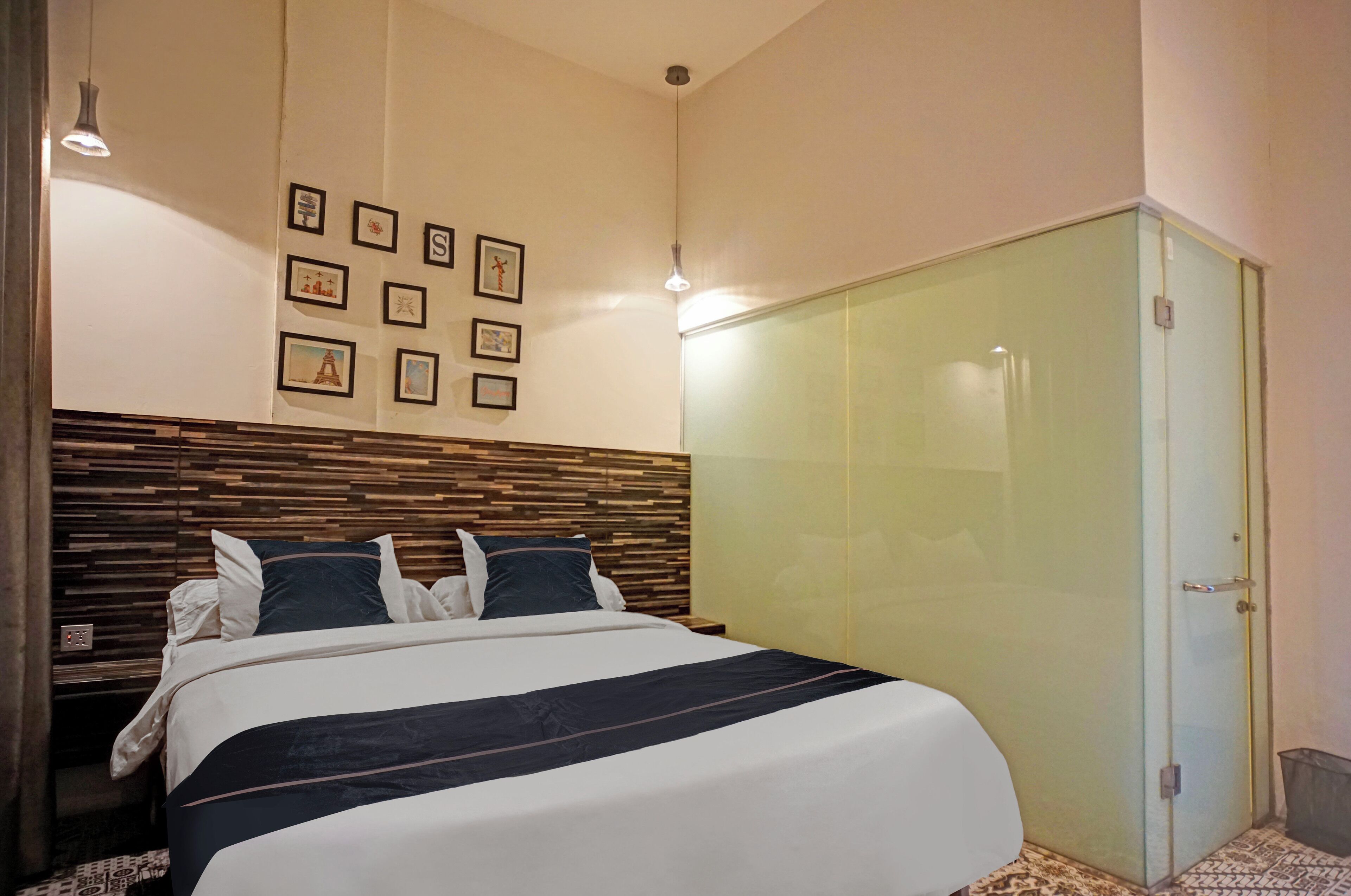 Un dormitorio con cabecera de madera, cama con colcha a rayas negras y blancas, armario de cristal y cuadros enmarcados en la pared.