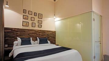 Un dormitorio con cabecera de madera, cama con colcha a rayas negras y blancas, armario de cristal y cuadros enmarcados en la pared.