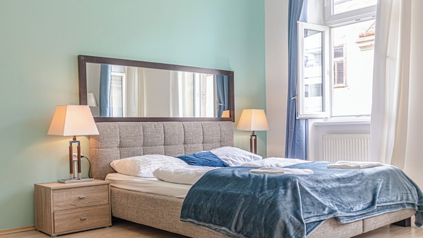 A neatly arranged bedroom with a bed, two bedside tables, a large mirror, and a window with curtains. - 2BR Apartment Long Stay Up to 6 Guests (Vienna)