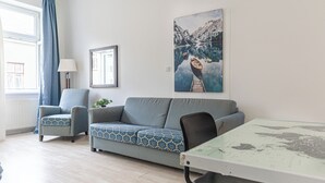 A modern living room with a sofa, armchairs, a glass coffee table, and a painting of a mountain lake. - 2BR Apartment Long Stay Up to 6 Guests (Vienna)