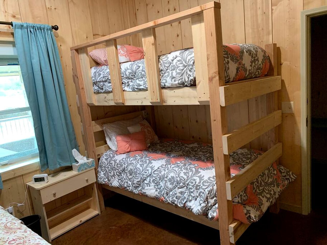 Un lit superposé avec une table de chevet et une fenêtre avec des rideaux.