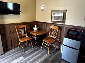 Una pequeña cocina americana equipada con microondas, refrigerador y una mesa de madera con sillas.