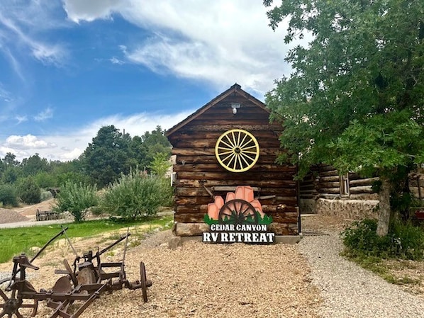 A rustic log cabin with a wheel symbol and text indicating a Cedar Canyon RV Retreat. - Rustic Cabin that Sleeps Three near Cedar Breaks National Monument, Cedar City, Utah (Cedar City)