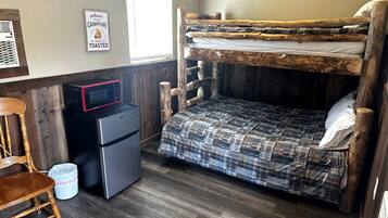 A bunk bed with a plaid bedspread, a small refrigerator, a microwave, a wooden chair, and a welcome sign.