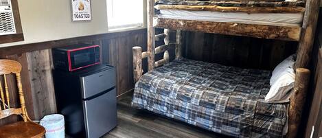 Ein Stockbett mit Karo-Bettdecke, ein kleiner Kühlschrank, eine Mikrowelle, ein Holzstuhl und ein Willkommensschild.