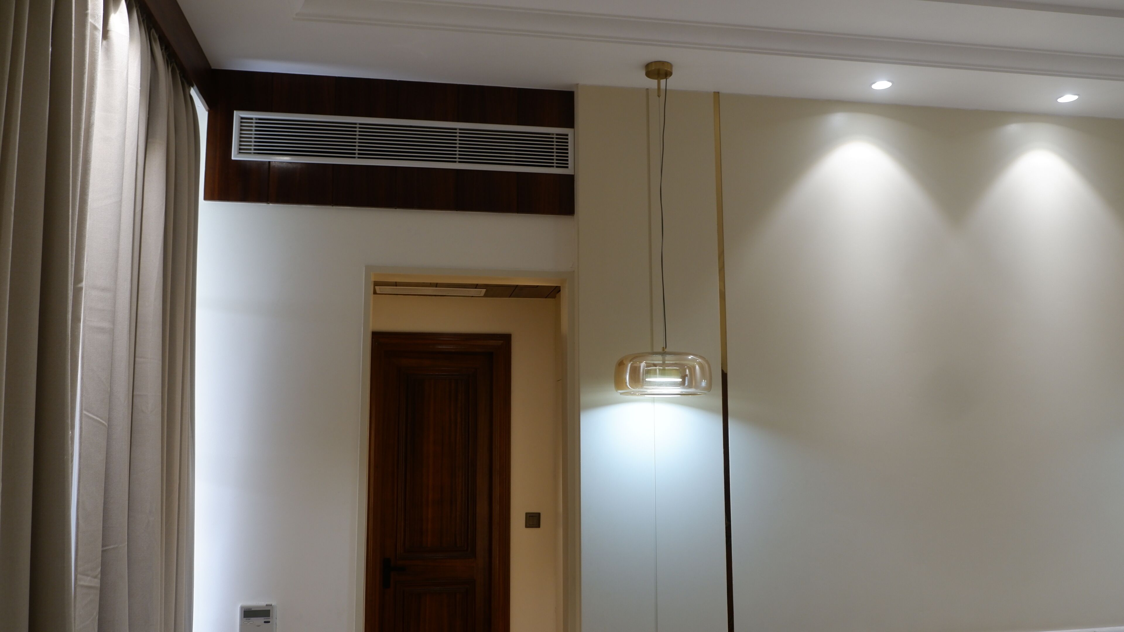 A room with a wooden door, a ceiling vent, and a pendant light.