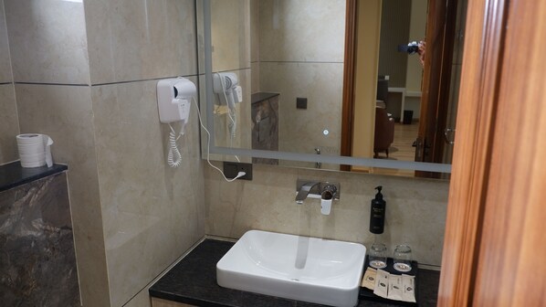 Une salle de bain avec un lavabo blanc, un miroir, un sèche-mains et un distributeur de serviettes en papier.