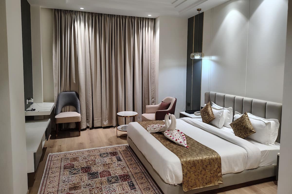 Habitación de hotel con una cama, dos sillones, una mesita, un escritorio y un ventanal con cortinas.