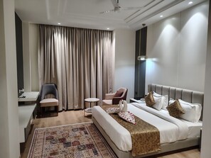 Een hotelkamer met een bed, twee fauteuils, een kleine tafel, een bureau en een groot raam met gordijnen.