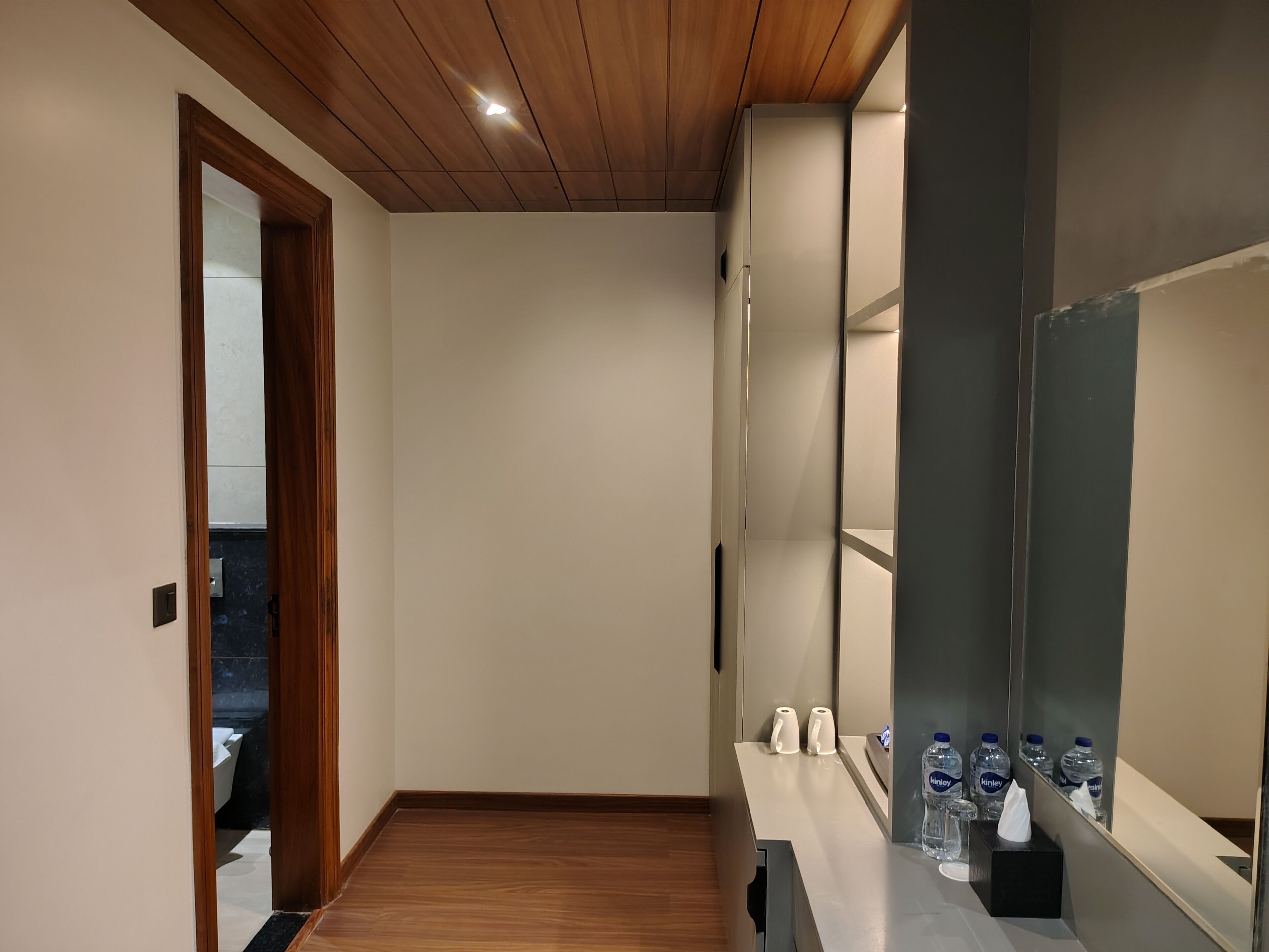 Une salle de bain moderne avec un plancher en bois, un miroir et un comptoir sur lequel se trouvent des bouteilles d’eau et une boîte de mouchoirs.