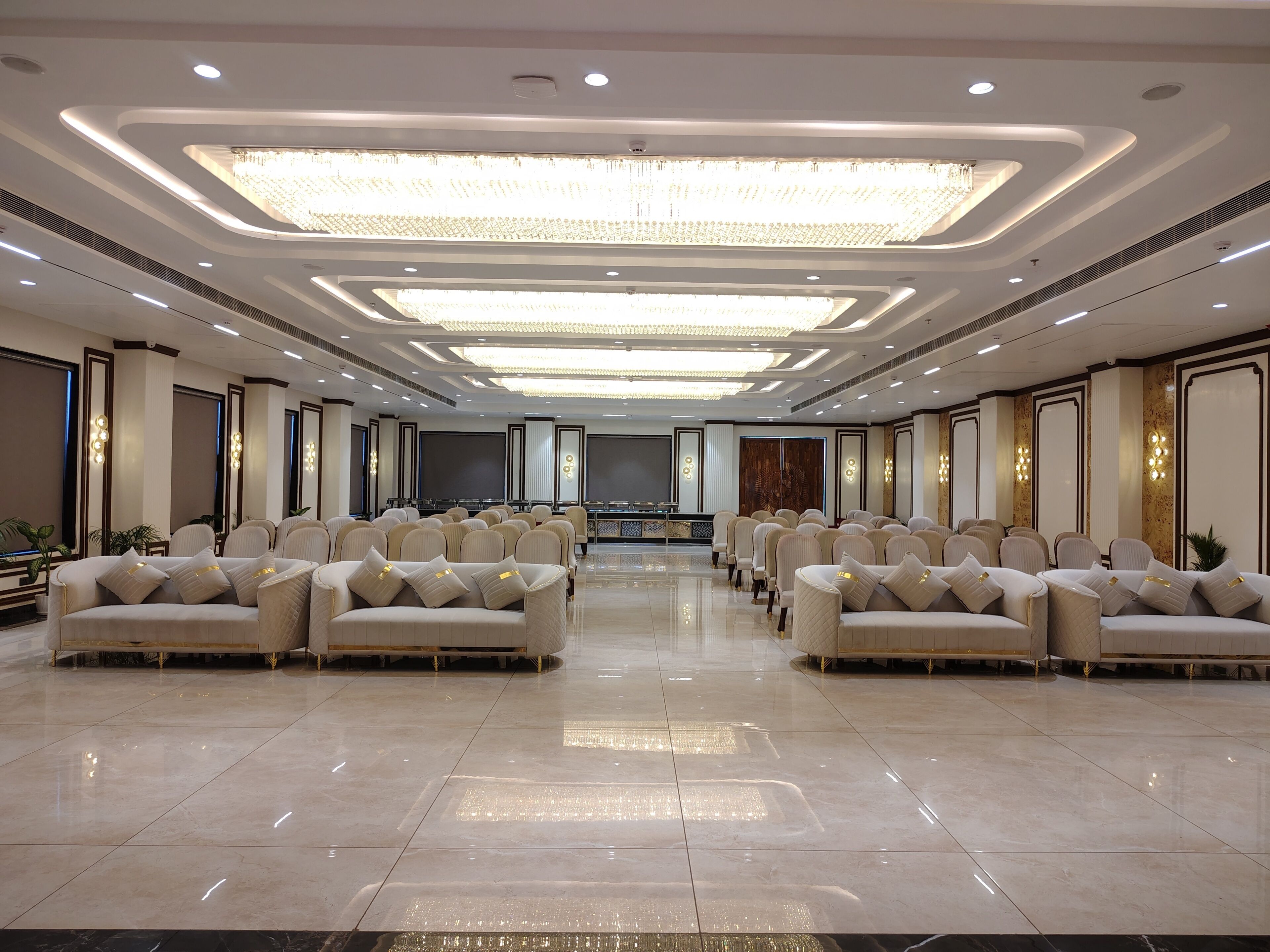 A spacious hotel conference room with rows of chairs, a stage, and a chandelier.