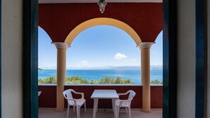 A balcony with a table and two chairs, overlooking a body of water and distant mountains.