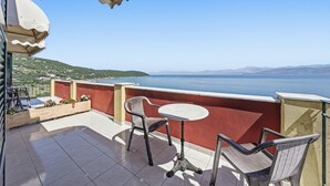 A balcony with a table and chairs, overlooking a body of water and distant mountains.