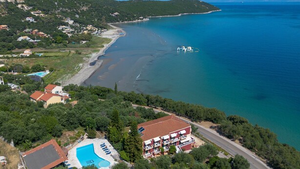 An aerial view of a coastal area with a swimming pool, a red-roofed building, and a beach.
