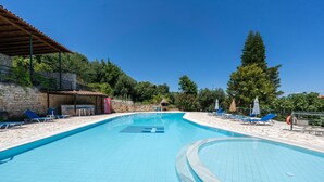A swimming pool with blue tiles, lounge chairs, and a stone building with a tiled roof.