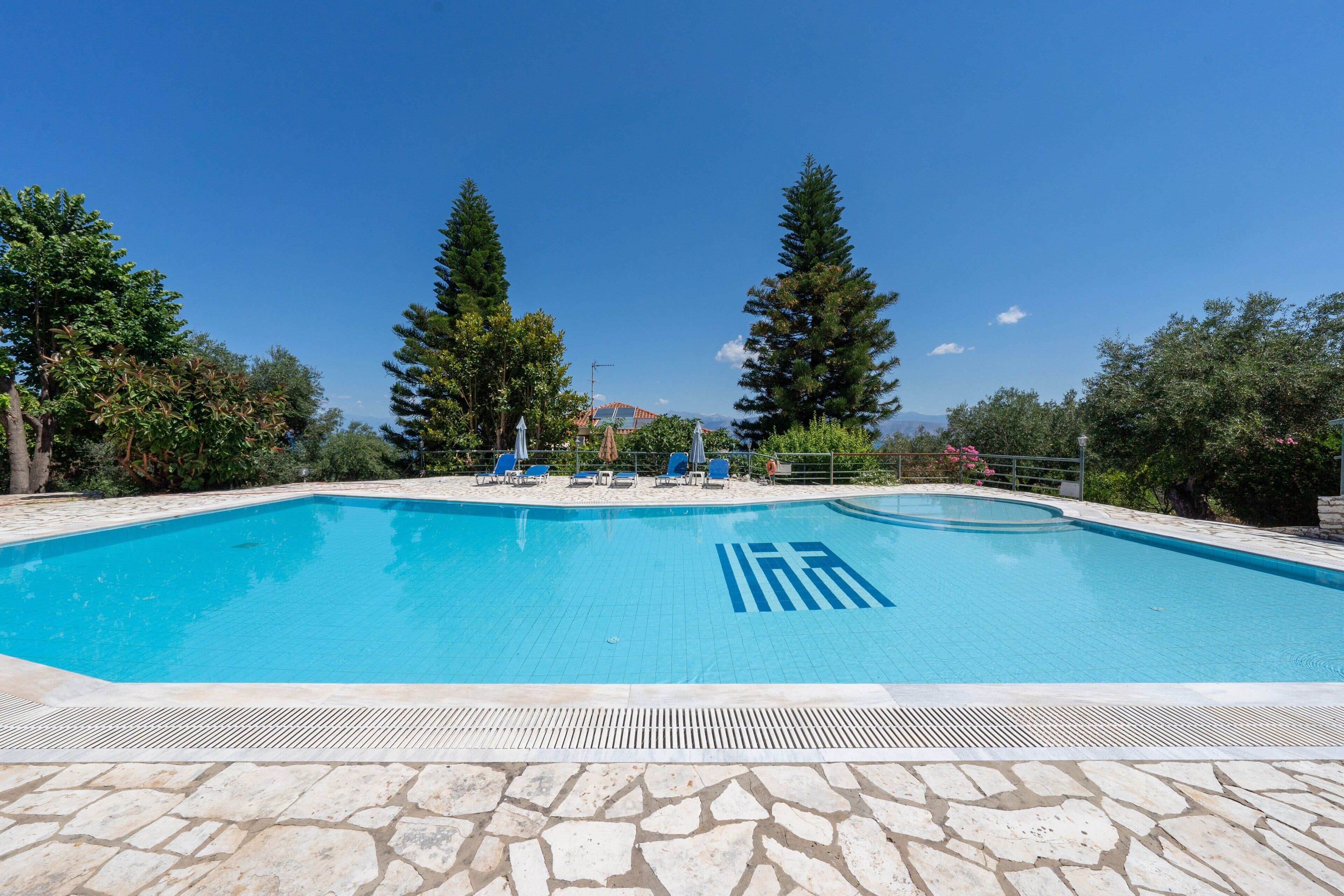 Une piscine dotée d’une plage en pierre, entourée d’arbres et surplombée par un ciel dégagé.