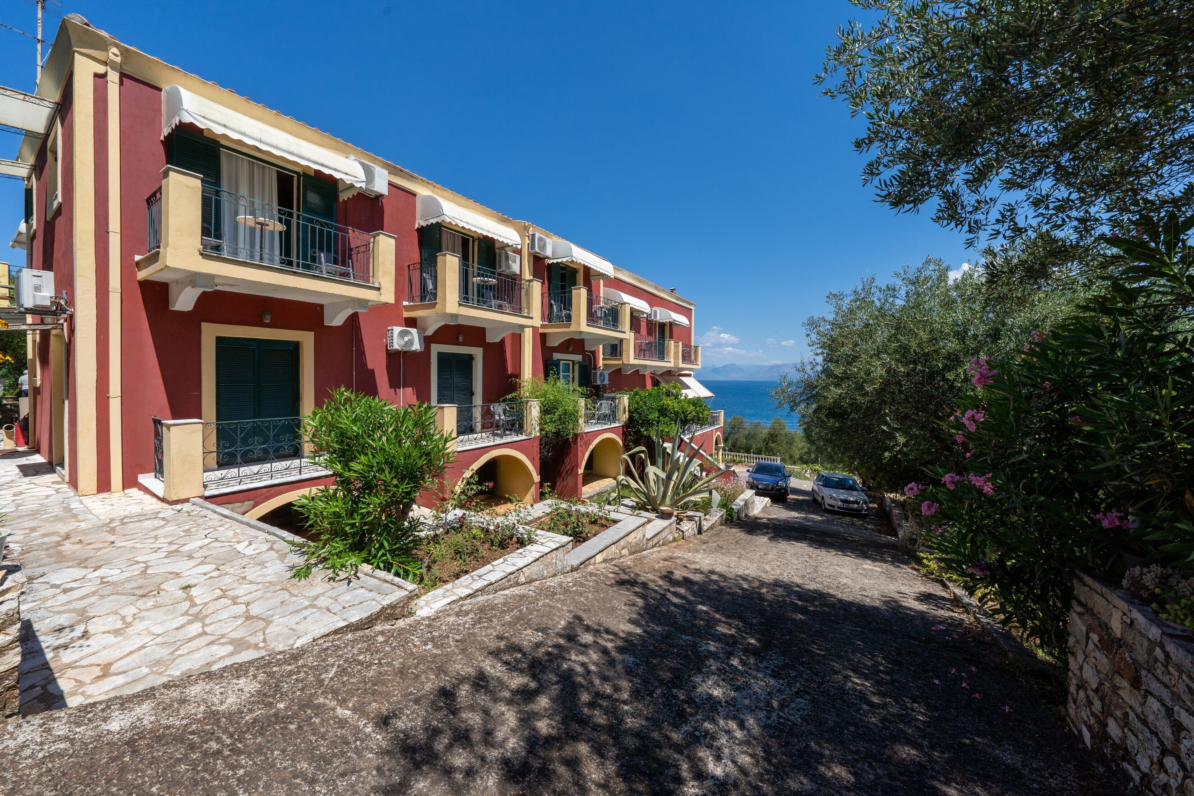 Un immeuble à plusieurs étages doté de balcons, d’une entrée pavée de pierres et offrant une vue sur la mer.