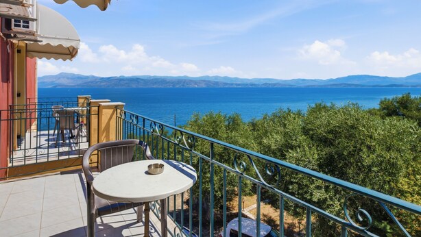 Ein Balkon mit Tisch und Stühlen mit Blick auf ein Gewässer und entfernte Berge.