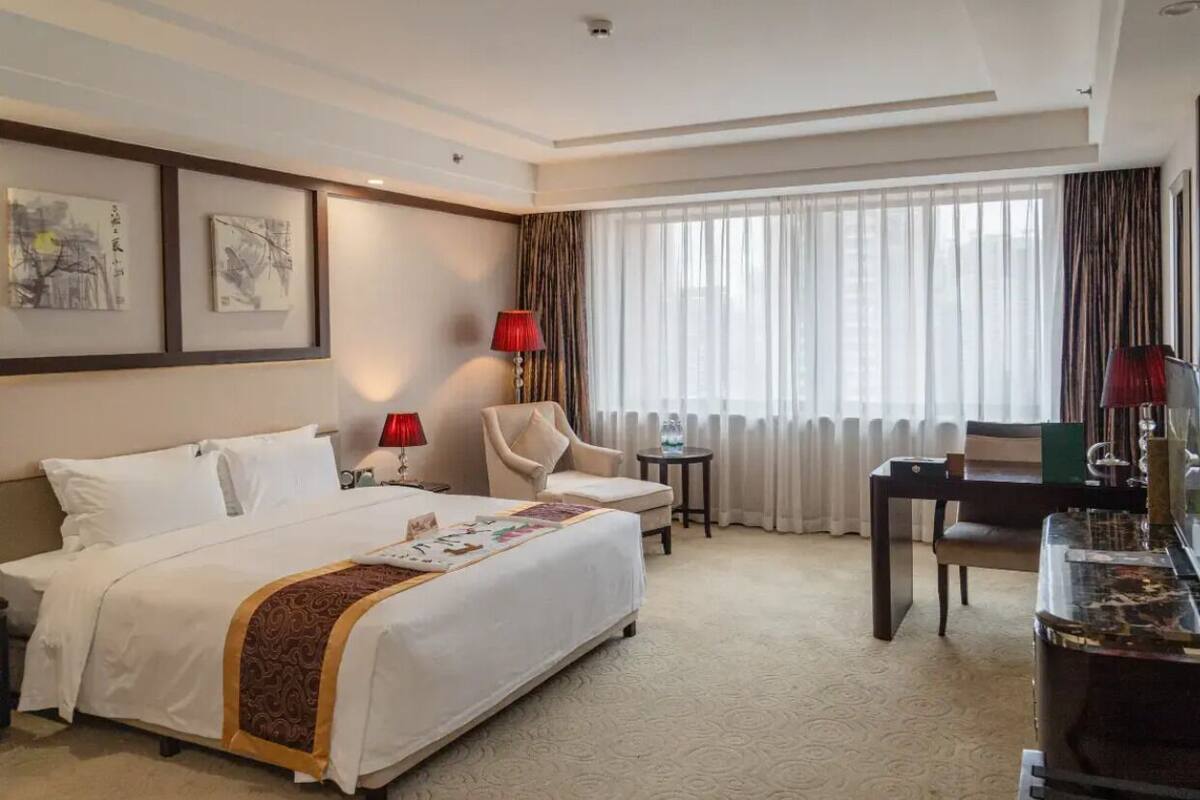 Habitación de hotel con cama, dos sillas, una mesita, una lámpara y una obra de arte en la pared.