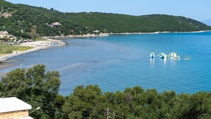 Blick auf die Küste mit Strand, klarem blauen Wasser und einem Hügel mit viel Grün.