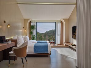 Una habitación de hotel moderna con una cama grande, un escritorio y vistas a una ladera boscosa.