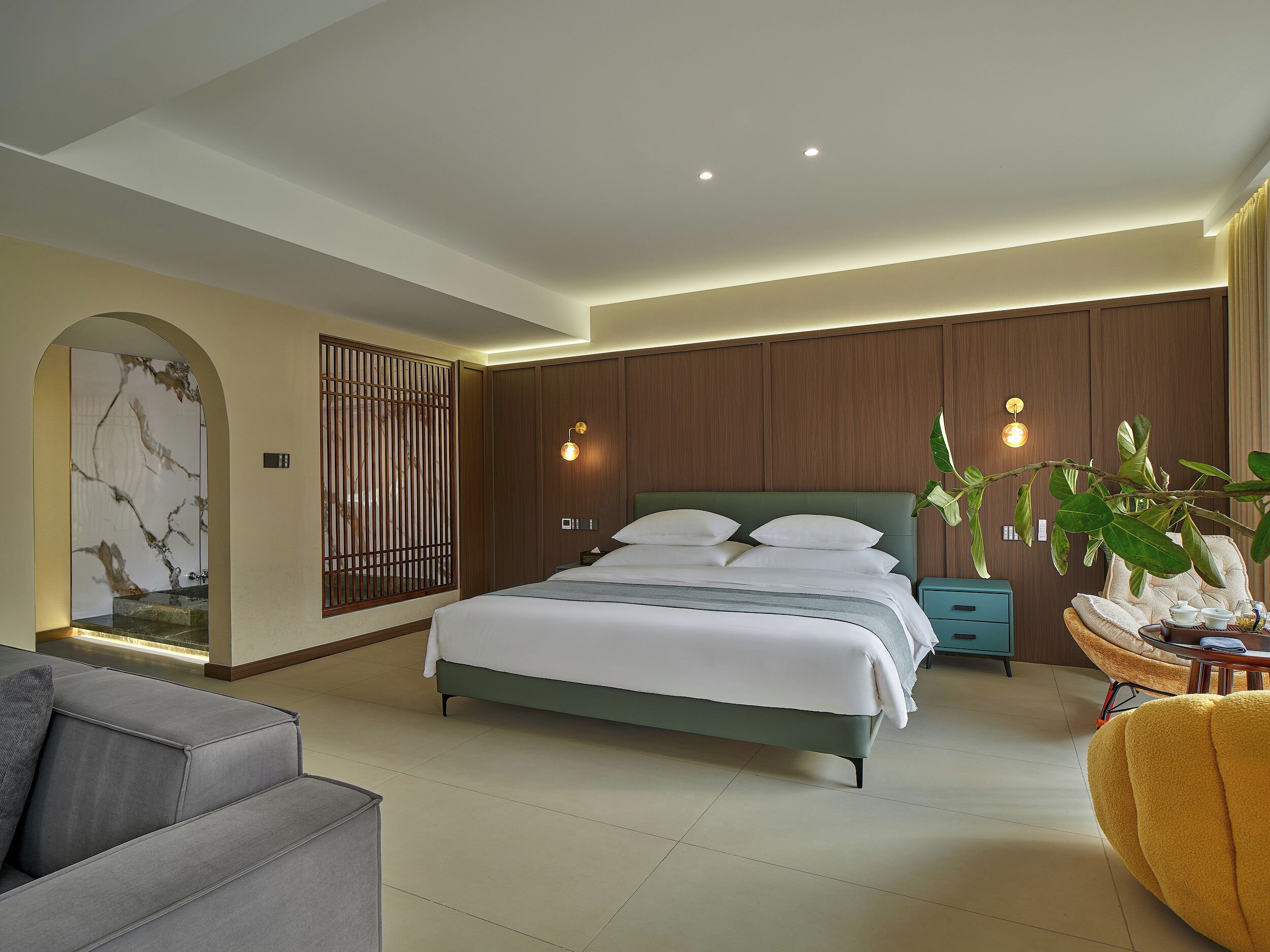 A modern bedroom with a large bed, a sofa, a nightstand, and a potted plant.