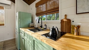 Una cocina con encimera de madera, refrigerador verde, hervidor negro y tabla de cortar de madera.