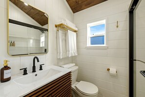 Ein Badezimmer mit weißem Waschbecken, Toilette, Spiegel und Fenster.