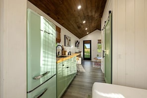 A kitchen with a green refrigerator, wooden ceiling, and a view to the outside.