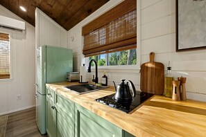 Eine Küche mit einer Holzausziehtafel, einem grünen Kühlschrank, einem schwarzen Wasserkocher und einem Schneidebrett.