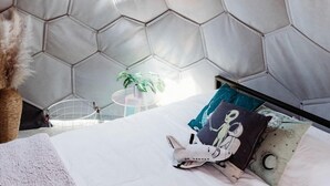 Una stanza con parete a motivo esagonale, un letto con cuscini e lampade a sospensione.