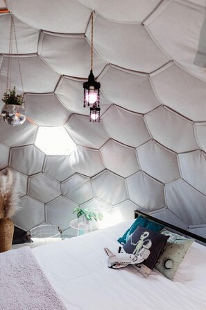 Una habitación con pared de diseño hexagonal, cama con almohadas e iluminación colgante.